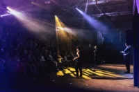 Performers on stage facing audience, illuminated by colourful stage lights